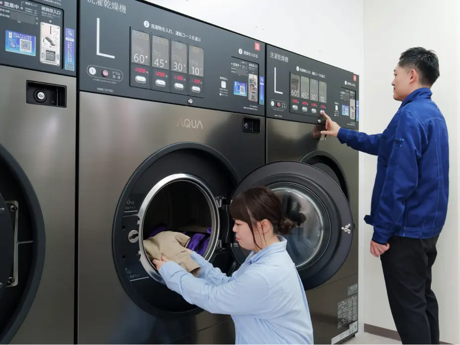 AQUA製の大型洗濯乾燥機を利用する男女の様子