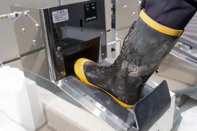 泥で汚れた作業用長靴を自動長靴洗浄機にかけて洗う様子