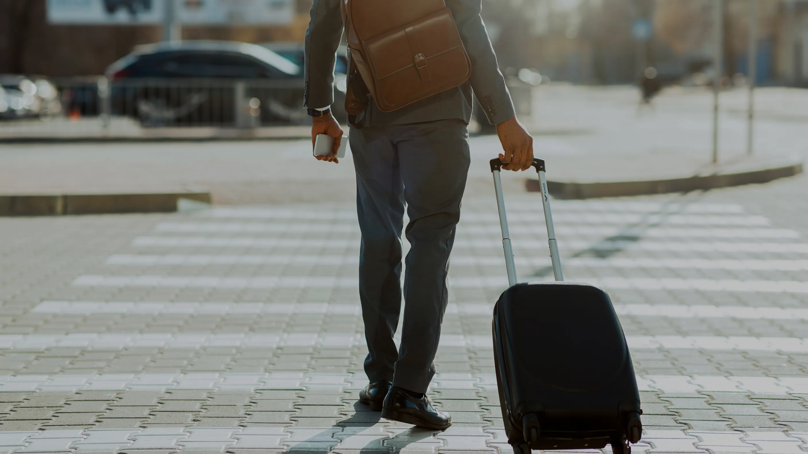 出張中のビジネスマンがスーツケースを引いて街中を歩く様子。