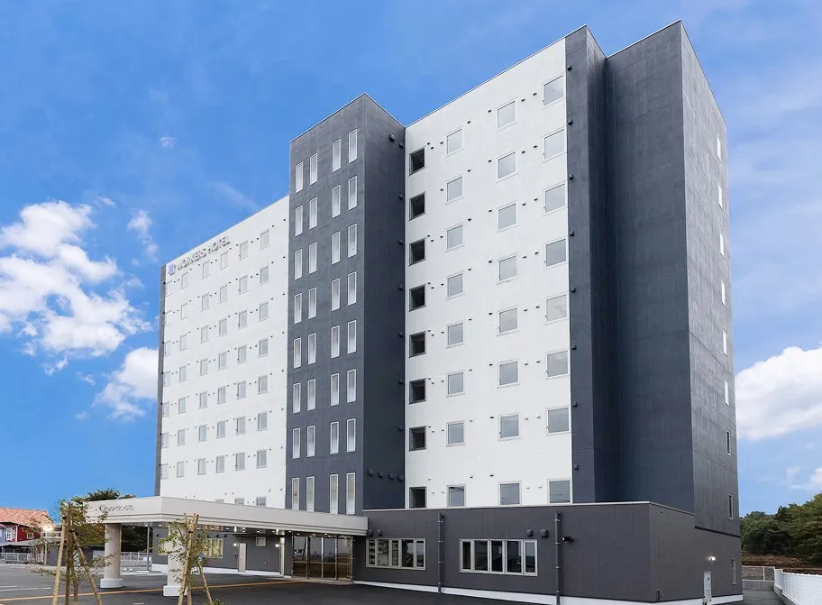 青空の下に建つ、白とグレーのモダンなホテル外観。