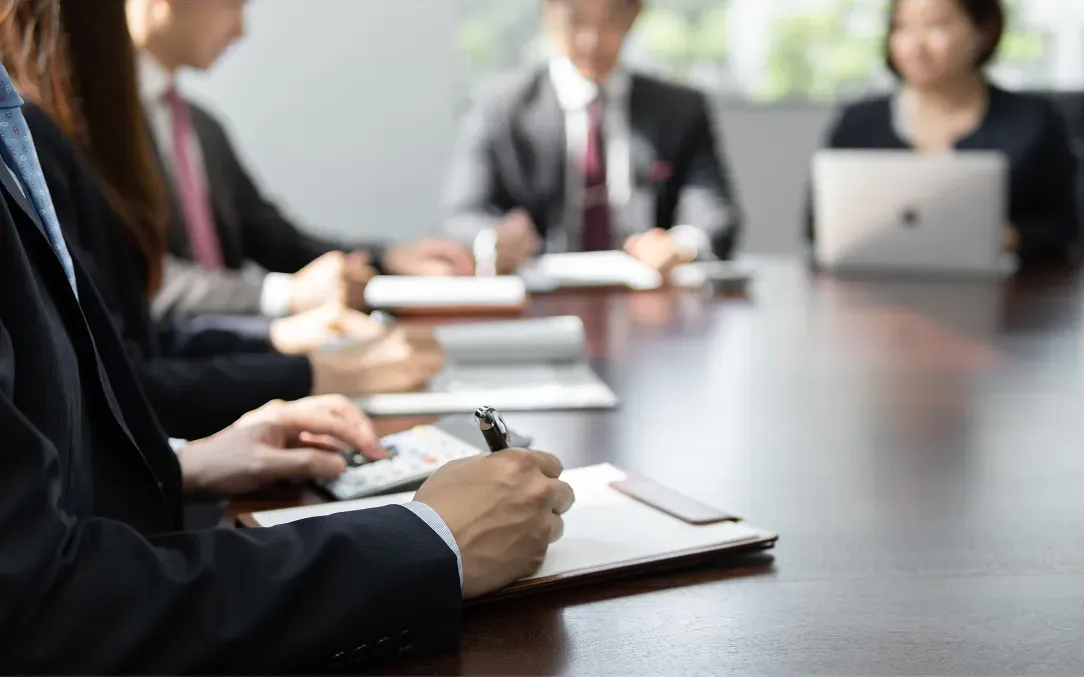 ビジネス会議の様子。参加者たちが資料にペンで書き込み、真剣な表情で打ち合わせを行っている。